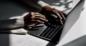 A dark-skinned hand, wearing a white long-sleeve blouse, typing on a silver and black laptop keyboard resting on a table.
Accessibility Training & Marketing